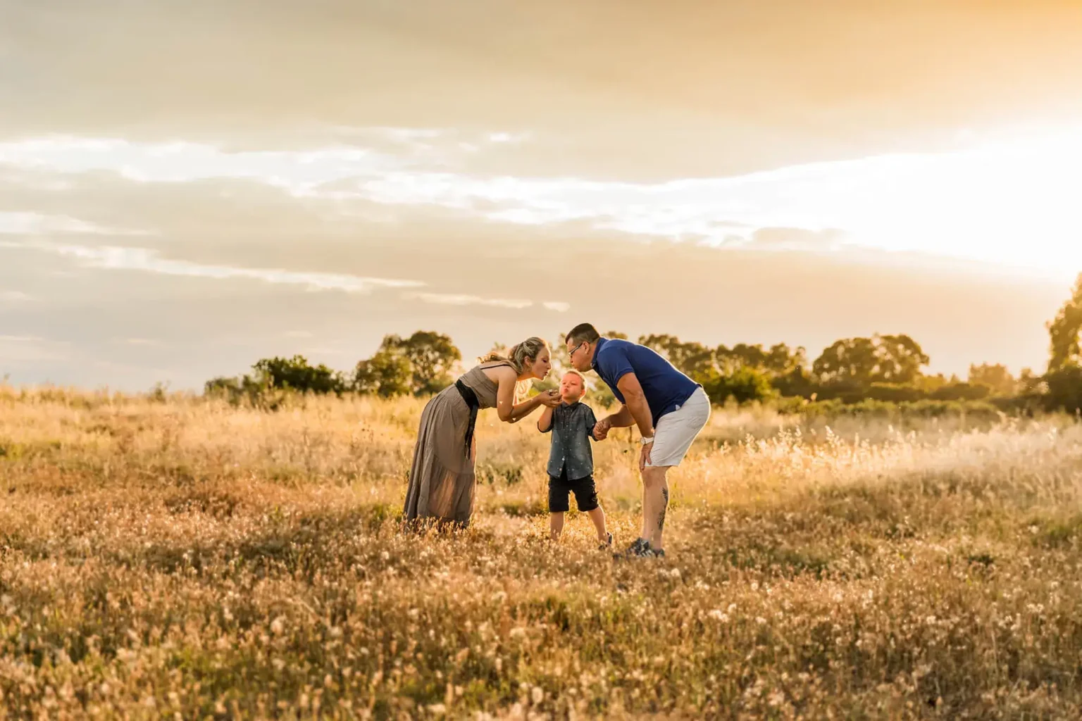 Servizio fotografico di famiglia all’aperto al tramonto, genitori e bambino in un campo naturale con luce calda e spontanea a san severo foggia
